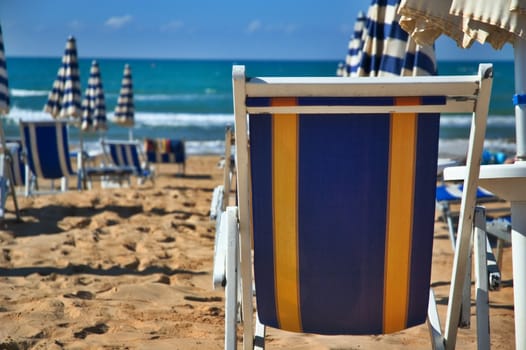 Empty deck chair and closed parasols on the beach on a windy day