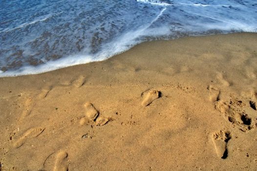 Footprints on sand and sea foam