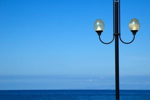 Lonely street lamp against blue sea and sky with copy space