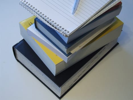 A stack of books with a note pad and pen on top.
