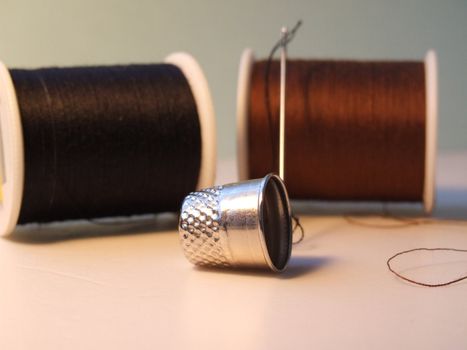 Silver thimble in focus in front of cotton reels and needle