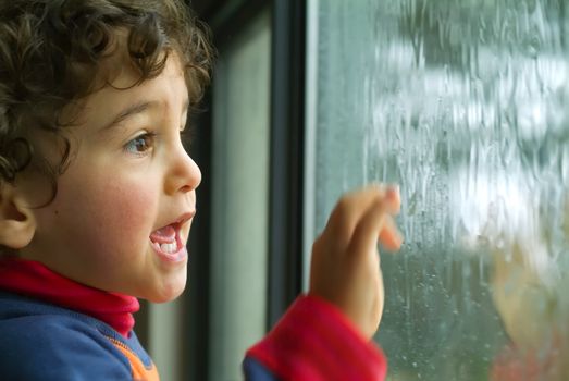 little boy watching the rain through the window