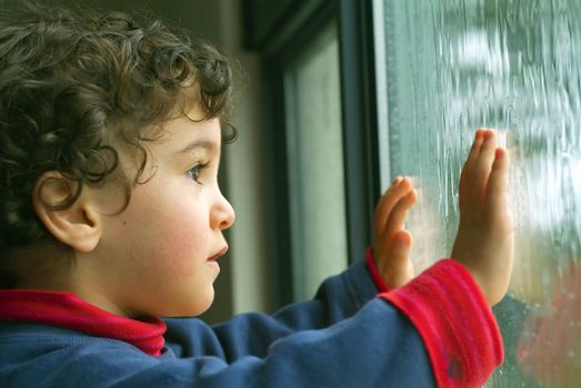 little boy watching the rain through the window