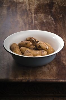 dirty potatoes in an old bowl on a wooden table