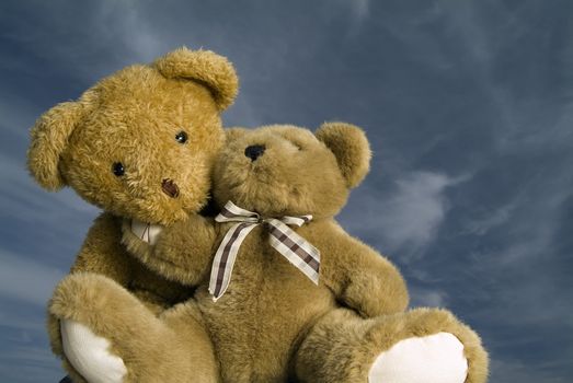two teddy bears hugging each other agaist blue sky with cirrus clouds