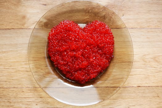 A lot of red caviar on a transparent plate in the form of heart