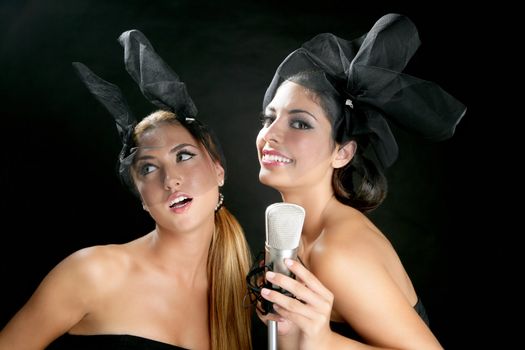 Beautiful women couple singing on a vintage microphone on black background