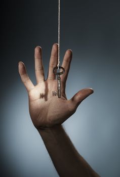 A Key hanging from a string in front of a hand.