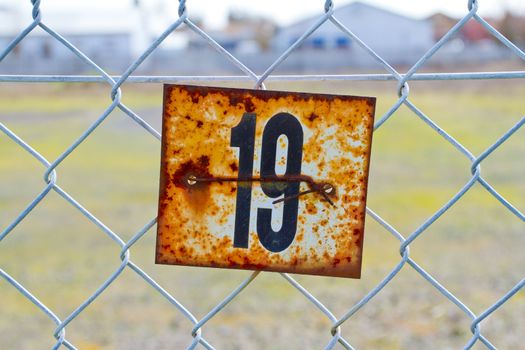 A series of rusted old signs or tags are attached to this chain link fence with orange and white rust and the numbers clearly visible.