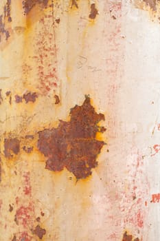Paint peels off this rusty weathered pole showing some muted tones of white pink orange and red.