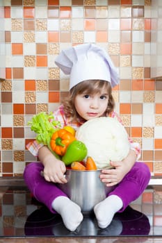 Baby cook with vegetables sits on a kitchen table