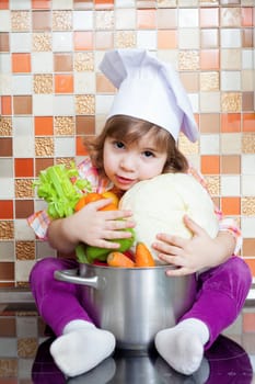 Baby cook with vegetables sits on a kitchen table