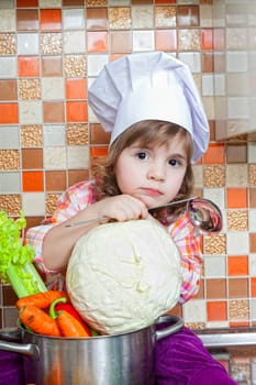 Baby cook with vegetables sits on a kitchen table