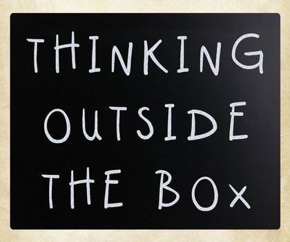 Thinking outside the box phrase, handwritten with white chalk on a blackboard