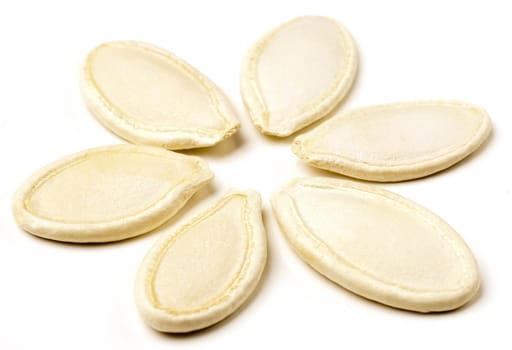 Pumpkin seeds arranged in flower shape on white background.