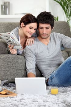 Couple sat on couch with newspaper and laptop