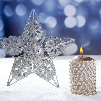 Christmas card of silver star and candle on snow and blue background