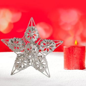 Christmas card of silver star and red candle on snow background