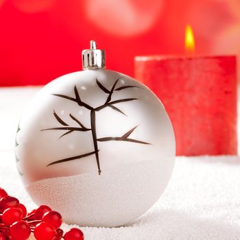 Christmas card of tree bauble and red candle on snow background