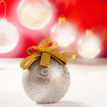 Christmas silver bauble with golden loop on snow red background