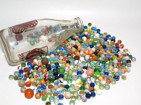 An assortment of various marbles and shooters spilled out next to a glass bottle.