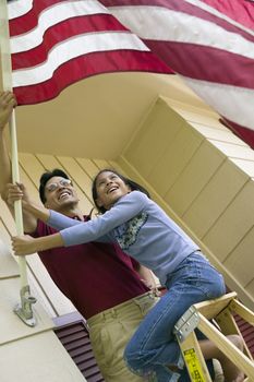 Smiling father and daughter put an American flag on their house