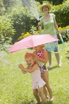 Smiling woman spaying little girls with water from a garden hose in the summertime