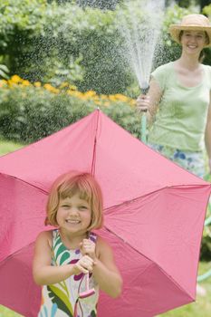 Smiling pretty woman spraying little girl with water from a garden hose in the Summertime
