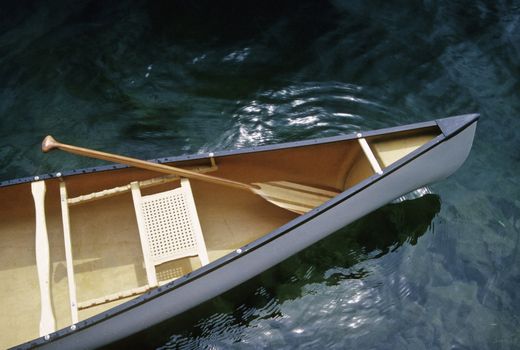 Canoe with paddle floating on clear water lake
