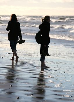 Two girlfriends barefoot go on wet sand