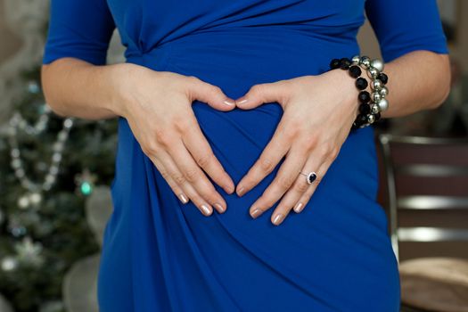 Young mother in blue dress making a heart shape with her hands against her belly.