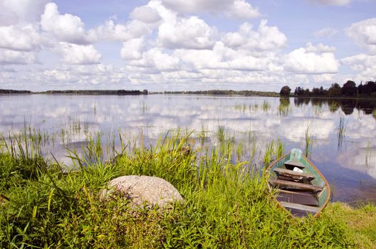 Lake fragment. Boats full of water resting near coast. Sky with clouds and reflections.