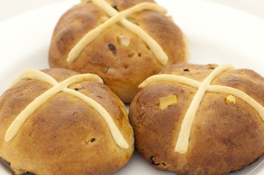 Cross bun with raisins and dried apricots on white plate