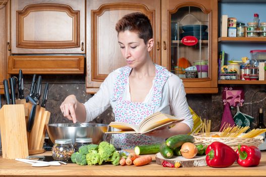 beautiful housewife cooking vegetables with cookbook in the kitchen