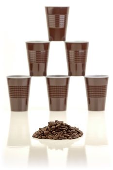 Pile of coffee beans and a stack of plastic cups arranged in the background on white.