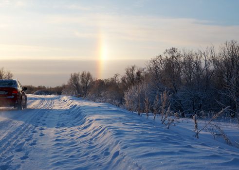 Road in a countryside in sunny winter rainbow day.Frozen trees in snowy field