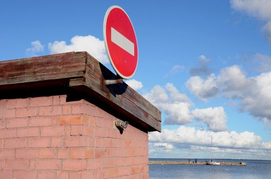 Road sign brick on building. Pier and sea visible in distance.