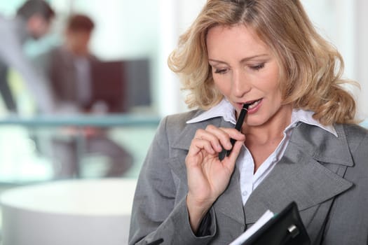 Pensive blond businesswoman chewing on pen