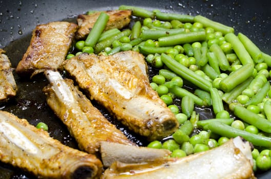 Pork ribs with peas and green beans prepared in a frying pan