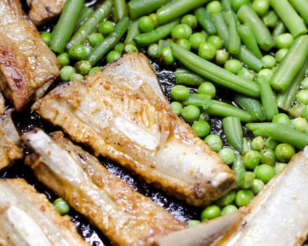 Pork ribs with peas and green beans prepared in a frying pan