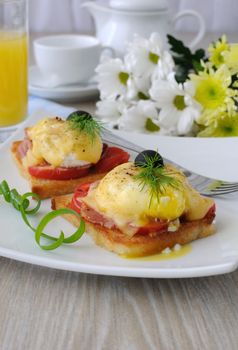 Eggs Benedict with ham and tomato and cheese on toast with orange juice and coffee