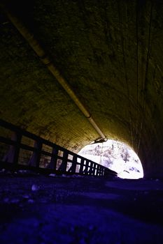 A ground level perspective of a tunnel, with tinted color.  The light at the end of the tunnel can be seen. 