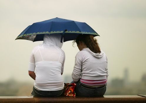 Two girls under dark blue umbrella on a background of the evening sky