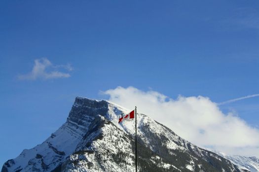 Canadian Flag flying over the snowy Rocky Mountains with sky and clouds