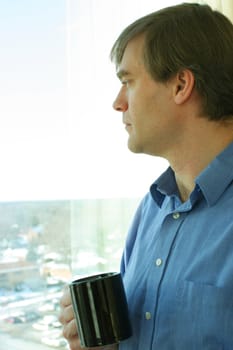 Handsome businessman standing by window thinking while drinking coffee.