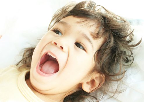 Beautiful toddler boy lying on bed laughing and smiling. Part asian, scandinavian descent.