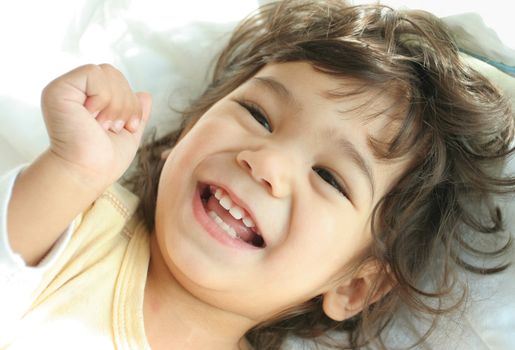 Beautiful toddler boy lying on bed laughing and smiling. Part asian, scandinavian descent.