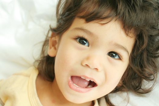 Beautiful toddler boy lying on bed laughing and smiling. Part asian, scandinavian descent.