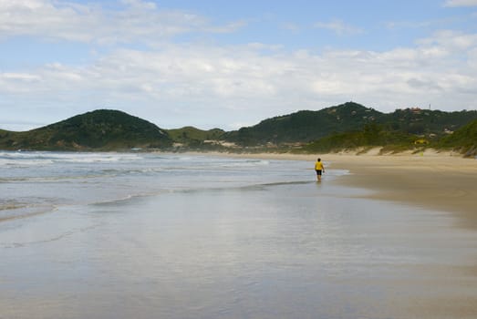 Woman walking alone on a deserted beach. Shot from behind.