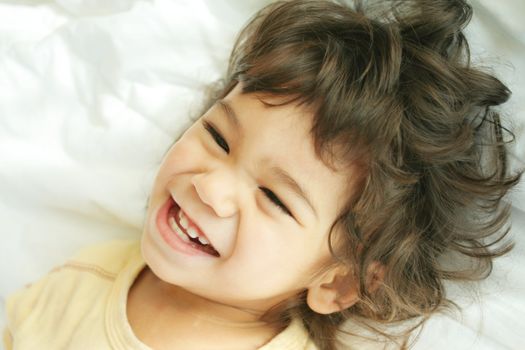 Beautiful toddler boy lying on bed laughing and smiling. Part asian, scandinavian descent.